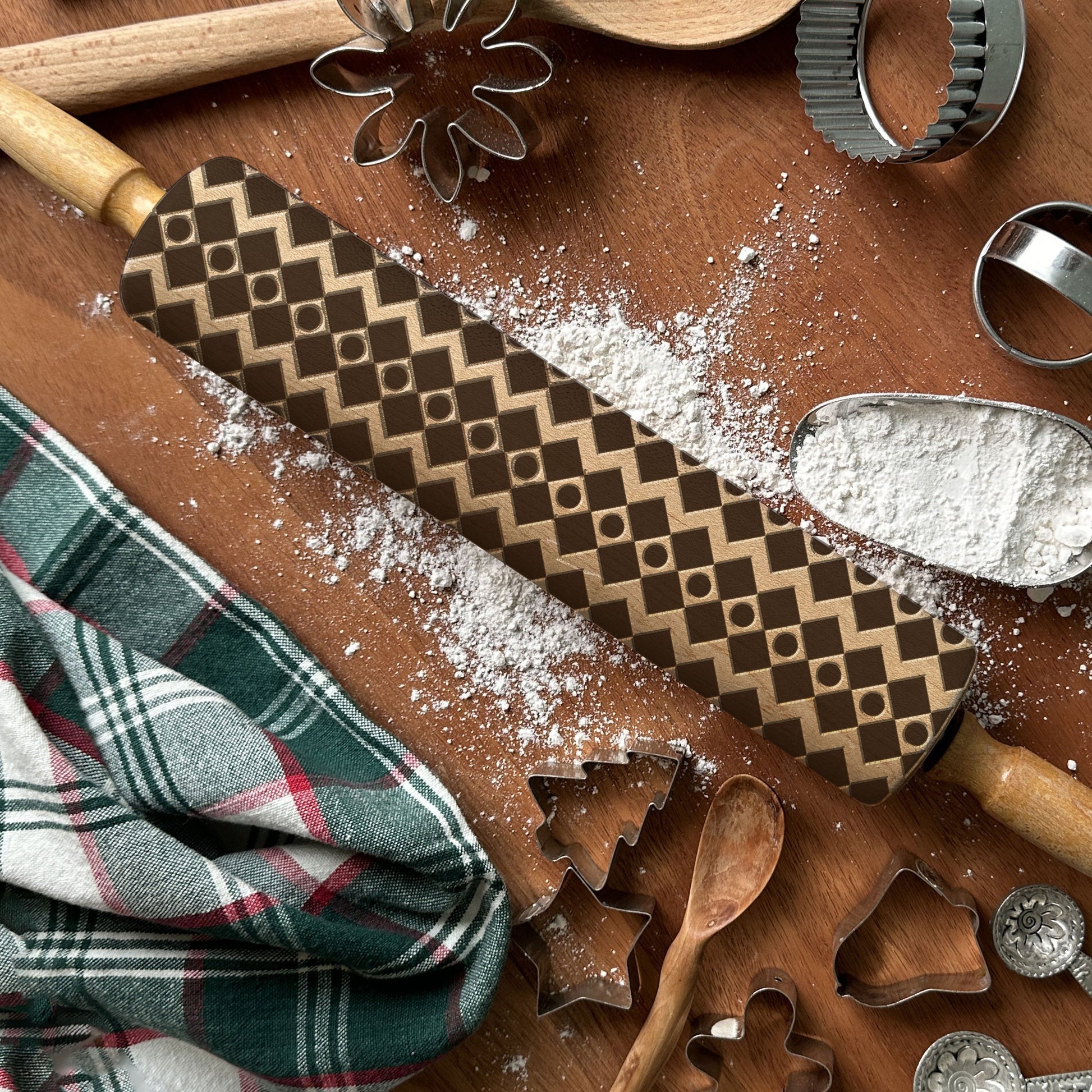 Baking tools including a patterned rolling pin, cookie cutters, and flour on a wooden surface.
