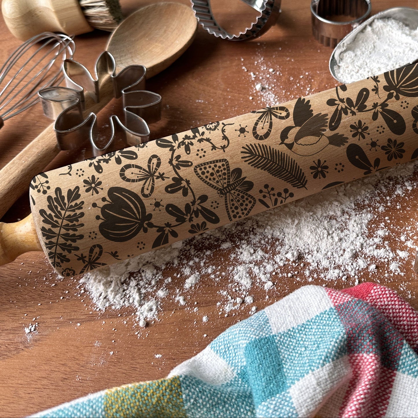 Decorative rolling pin with floral patterns on a wooden surface with baking tools.