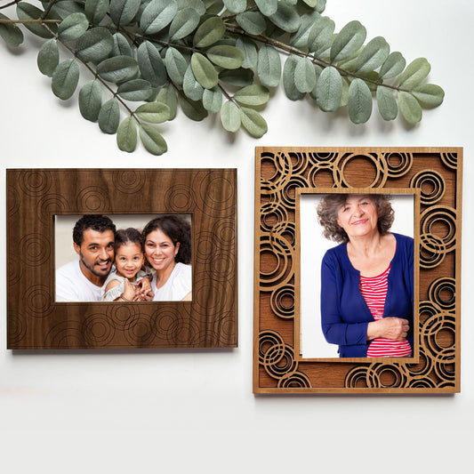 Two wooden photo frames with family portraits on a white background with green leaves.
