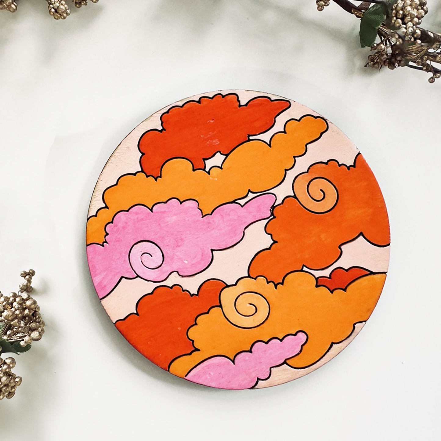 Round wooden coaster with colorful cloud design on a white surface