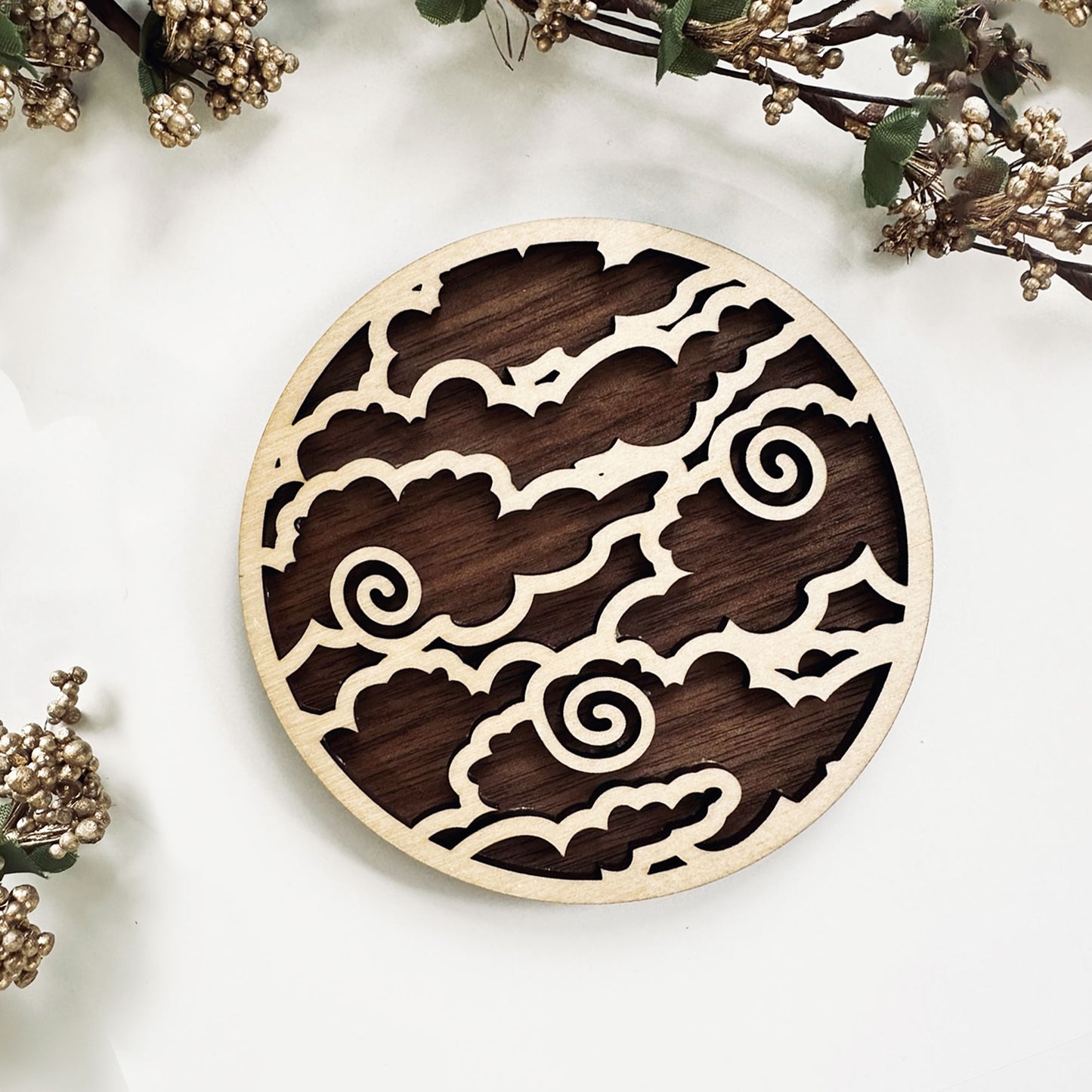 Wooden circular decorative coaster with laser-cut patterns on a white surface with decorative branches.