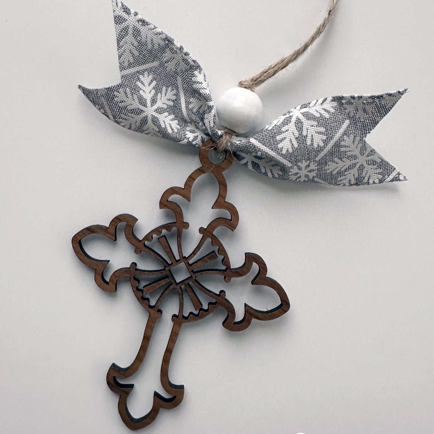 Decorative cross ornament with a gray ribbon featuring white snowflake patterns on a light gray background.