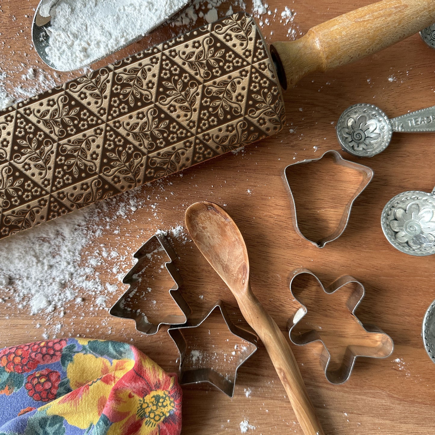 Decorative rolling pin and cookie cutters on a wooden surface with flour.