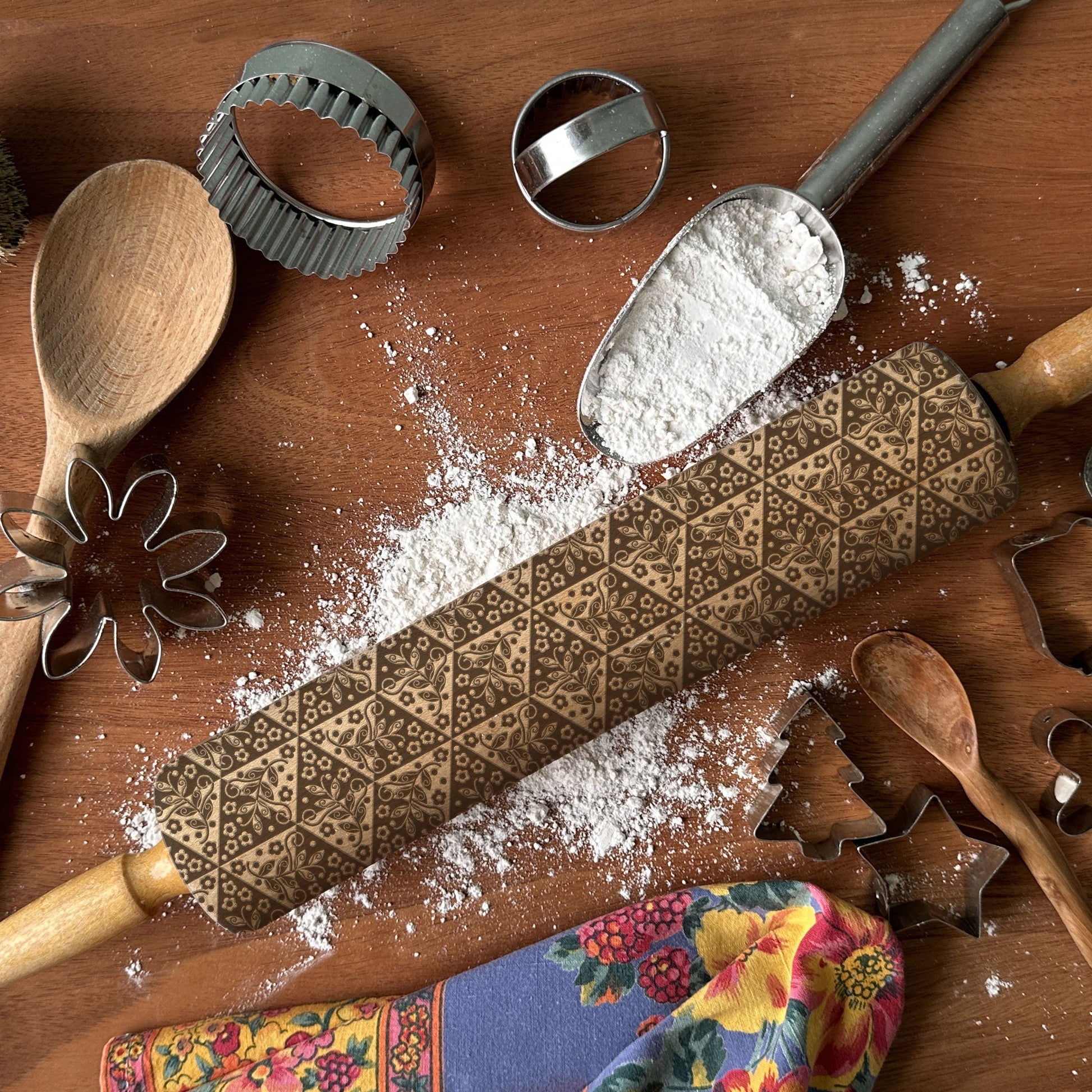 Baking tools including a rolling pin with a pattern, wooden spoon, and cookie cutters on a wooden surface.