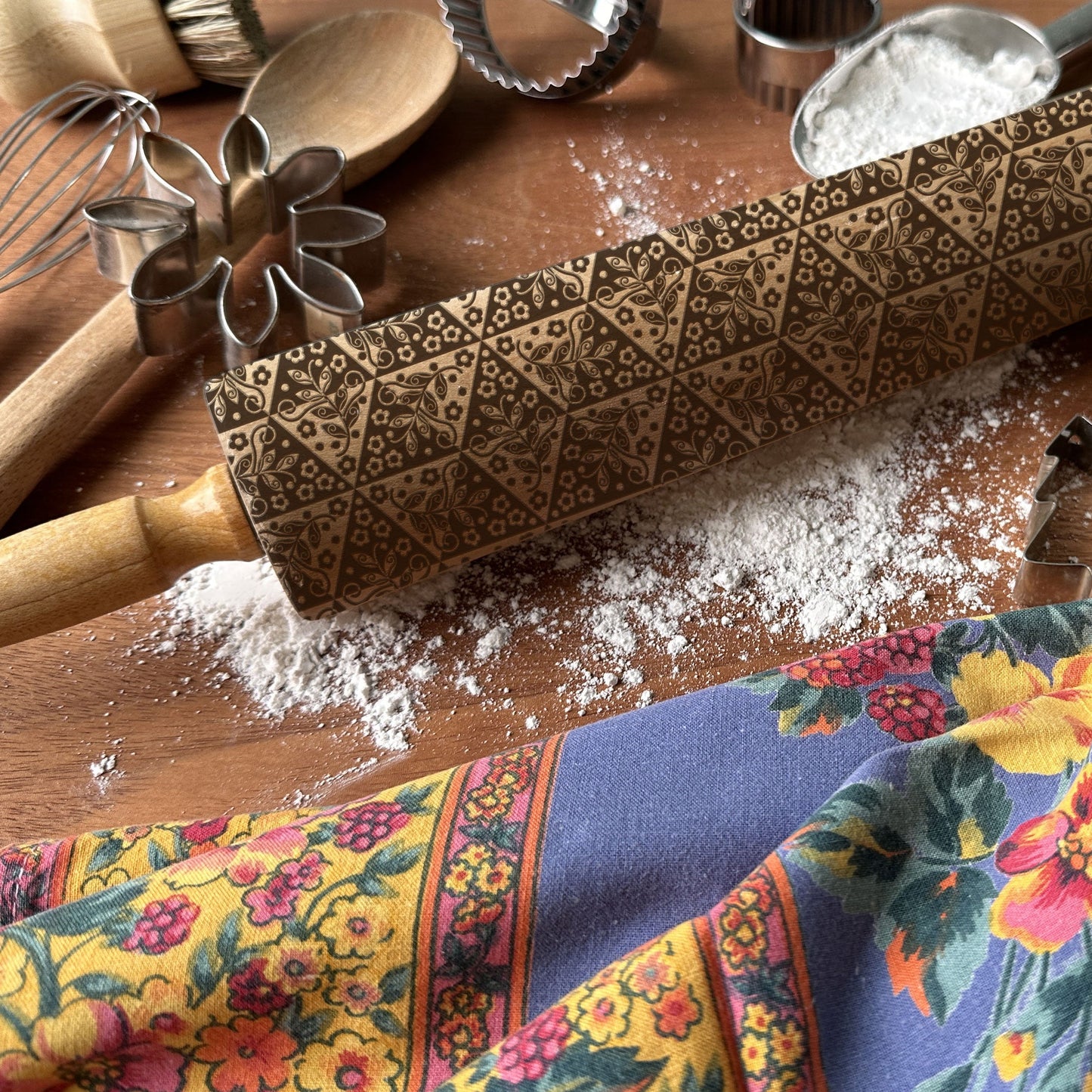 Decorative rolling pin with floral pattern on a wooden surface with baking tools and flour.