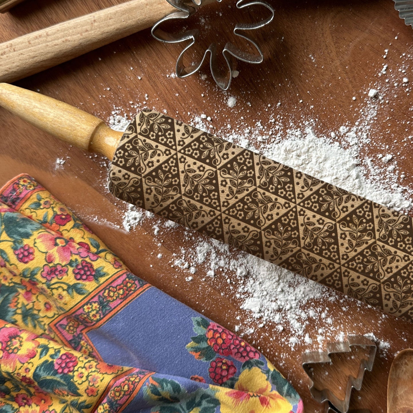 Decorative embossed rolling pin on a wooden surface with flour and baking tools.