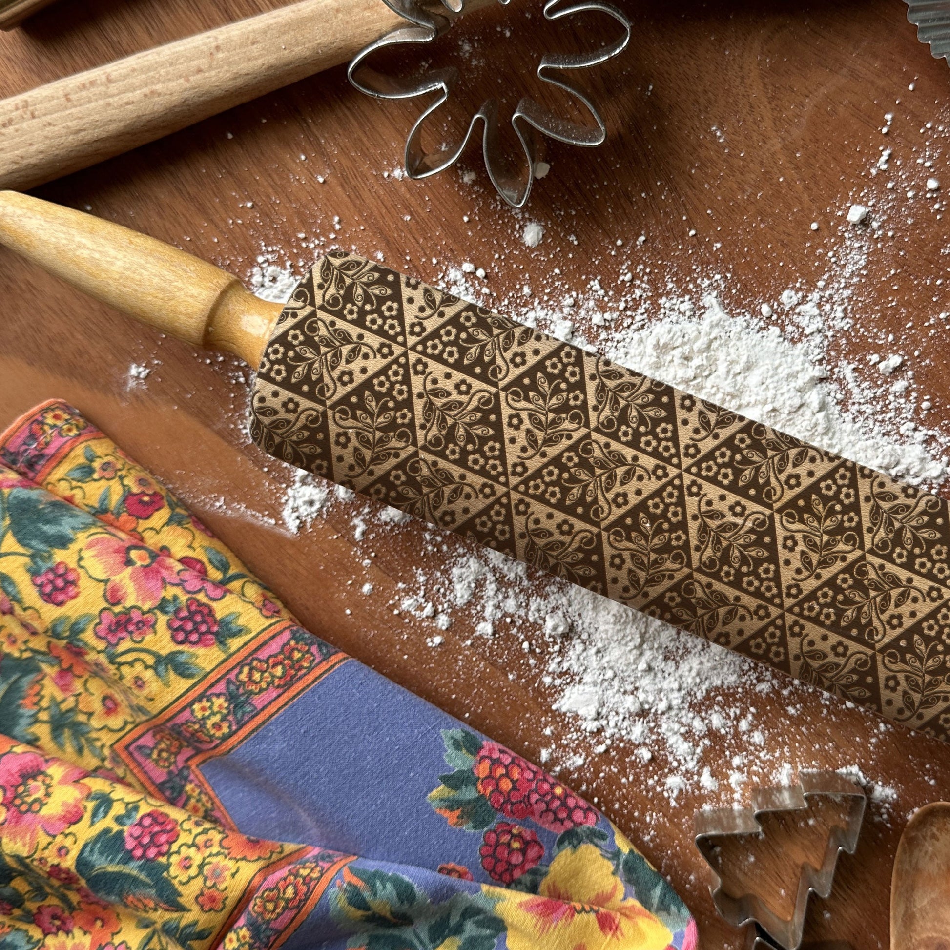 Decorative embossed rolling pin on a wooden surface with flour and baking tools.