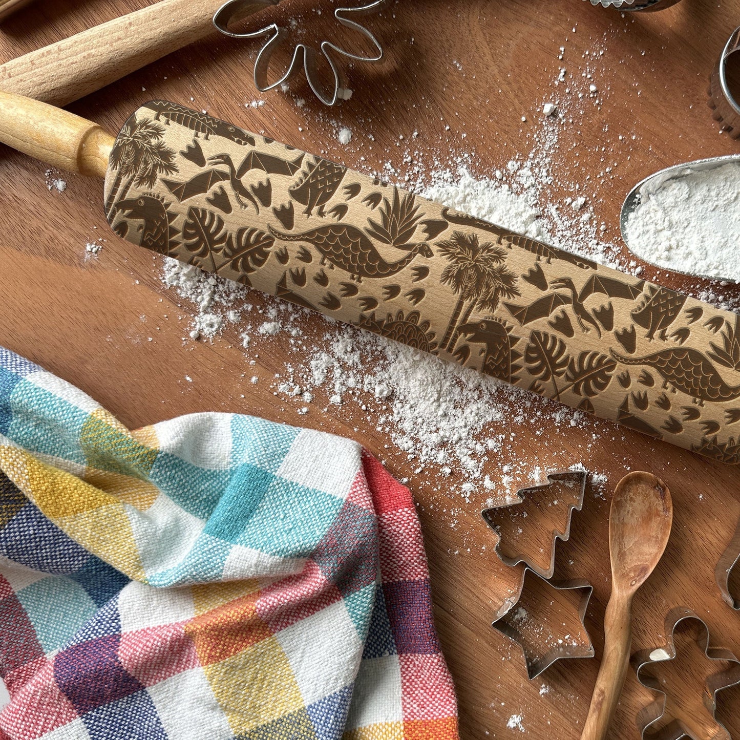 Decorative rolling pin with floral patterns on a wooden surface with cookie cutters and flour.