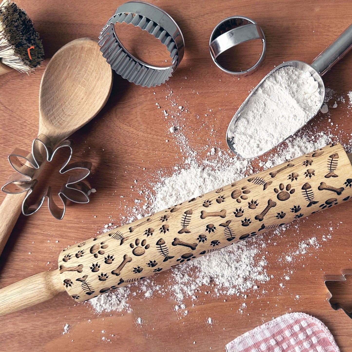 Wooden rolling pin with embossed designs on a wooden surface with flour and baking tools.