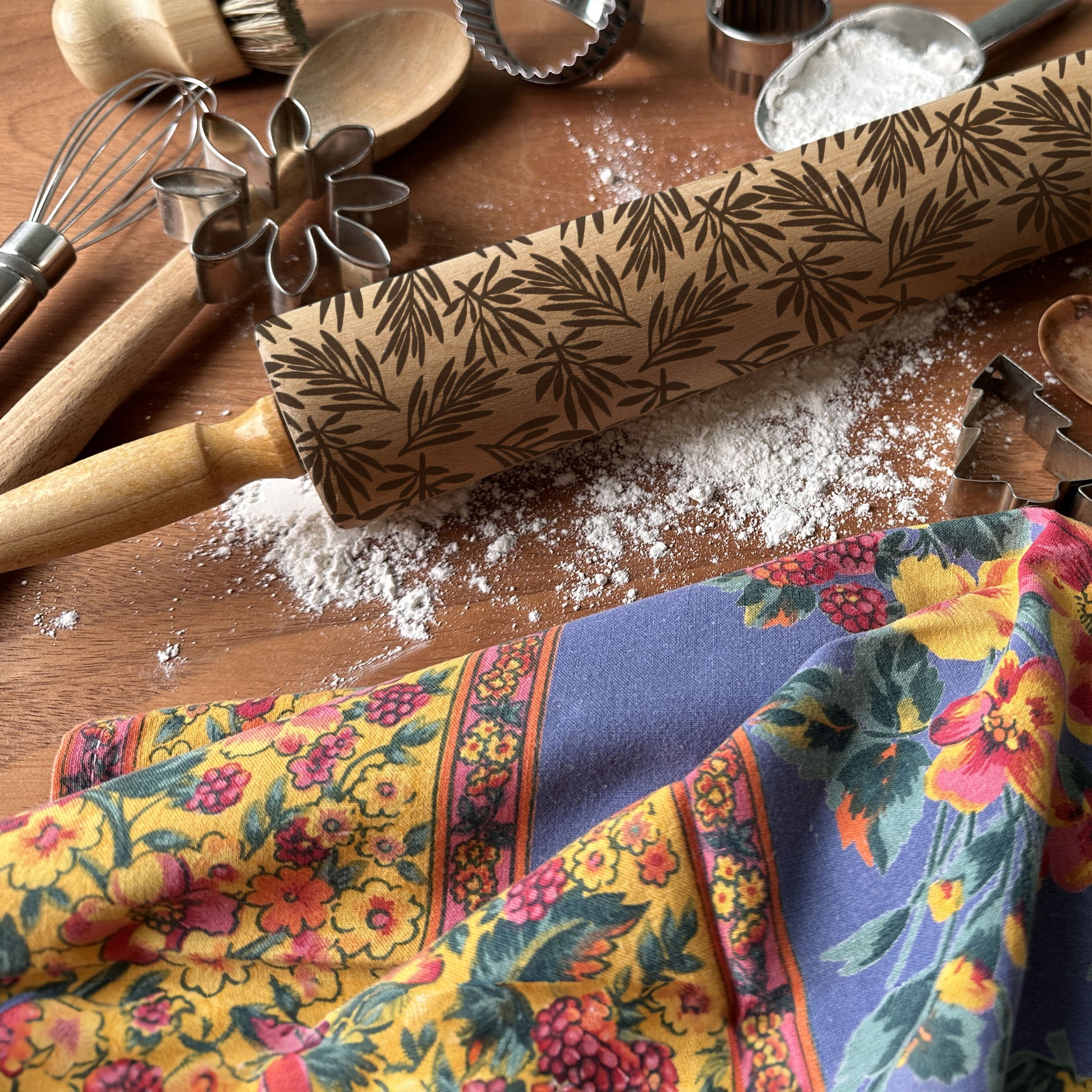 Floral-patterned rolling pin on a wooden surface with baking tools and flour.