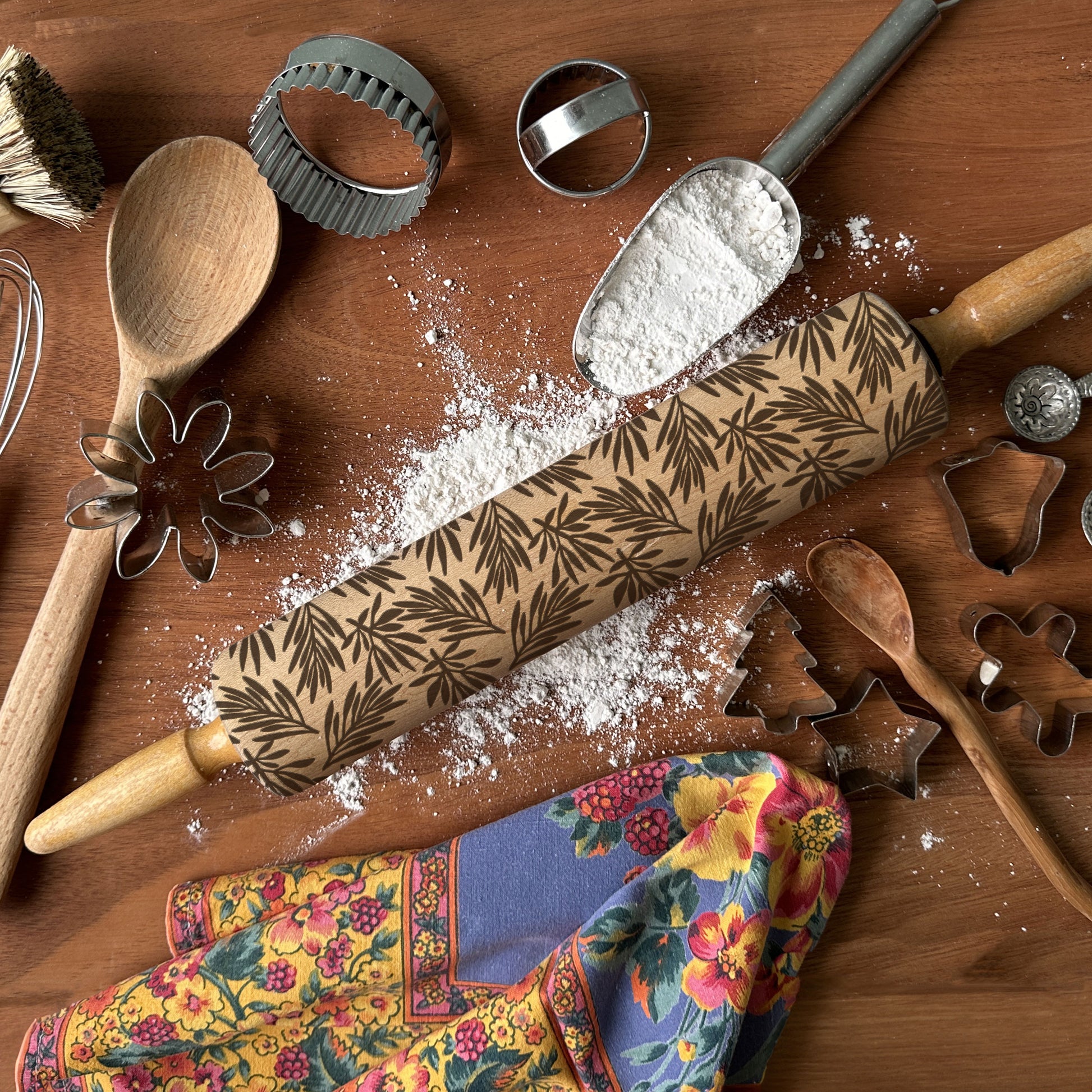 Wooden rolling pin with floral pattern on a wooden surface with flour and baking tools.