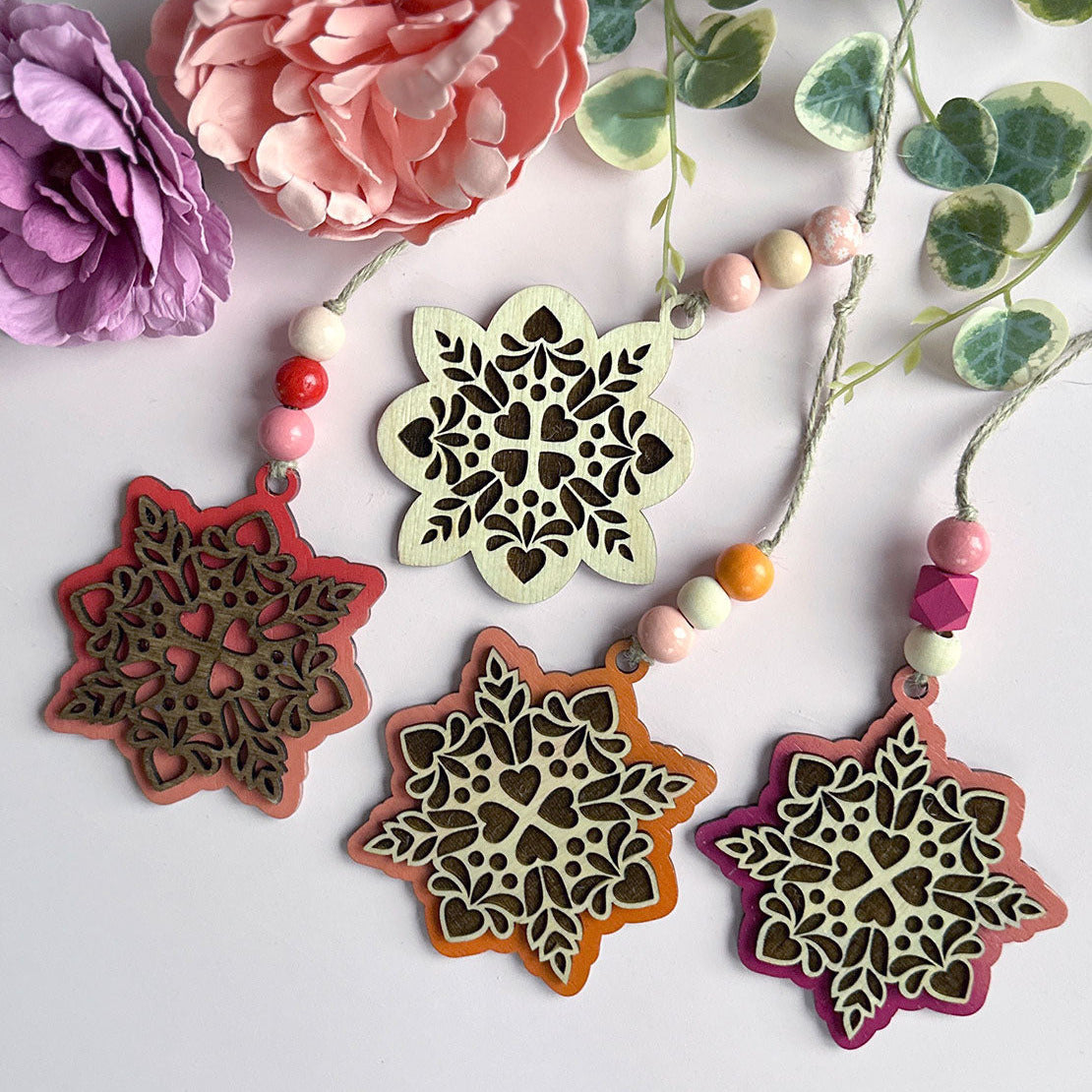 Decorative snowflake-shaped ornaments with beads on a white background with flowers and leaves.