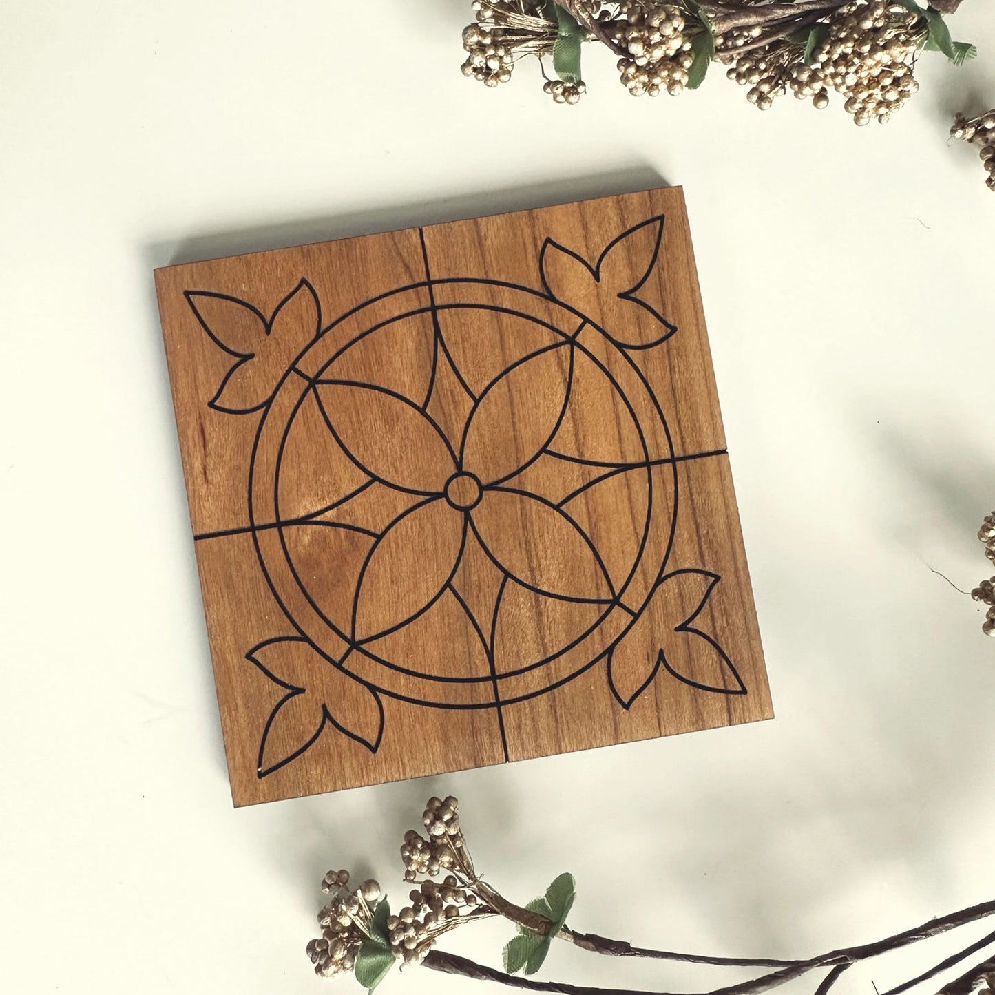 Wooden coaster with geometric design surrounded by decorative branches on a light background
