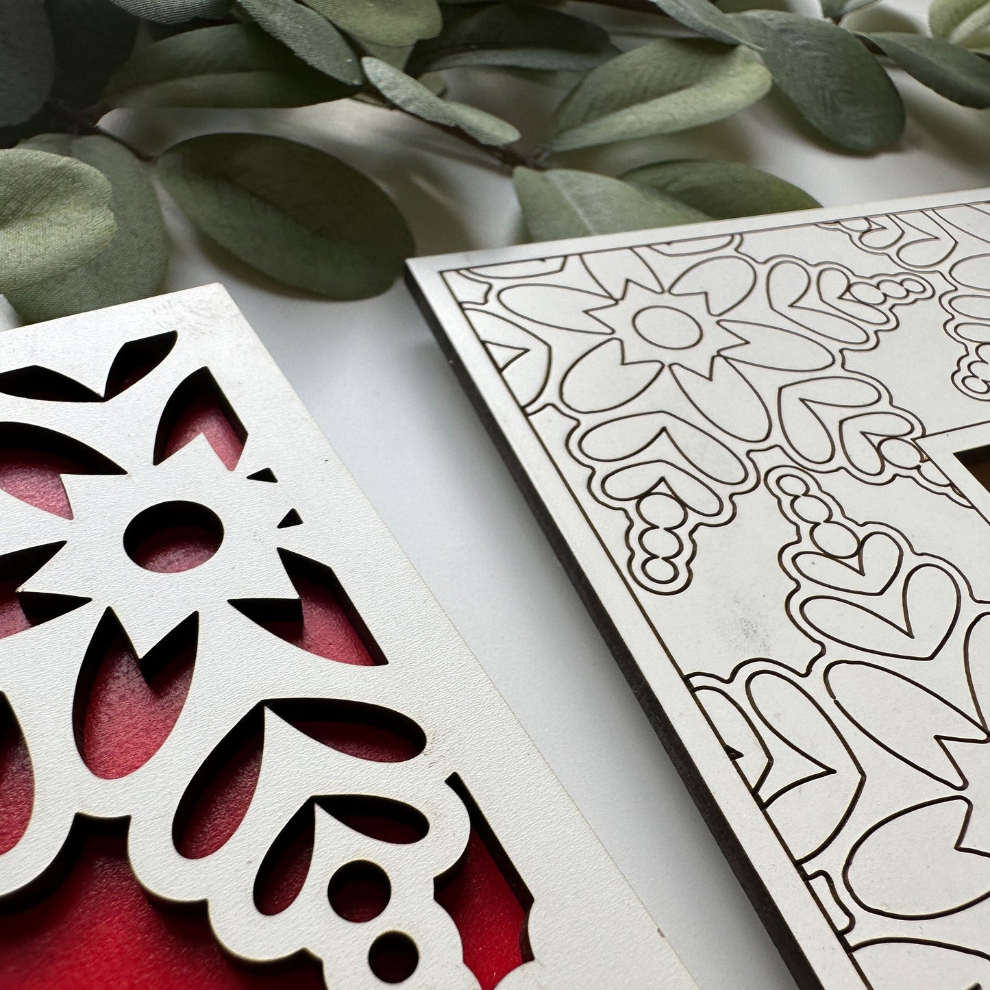 Decorative metal cutouts with floral patterns on a white surface with green leaves.