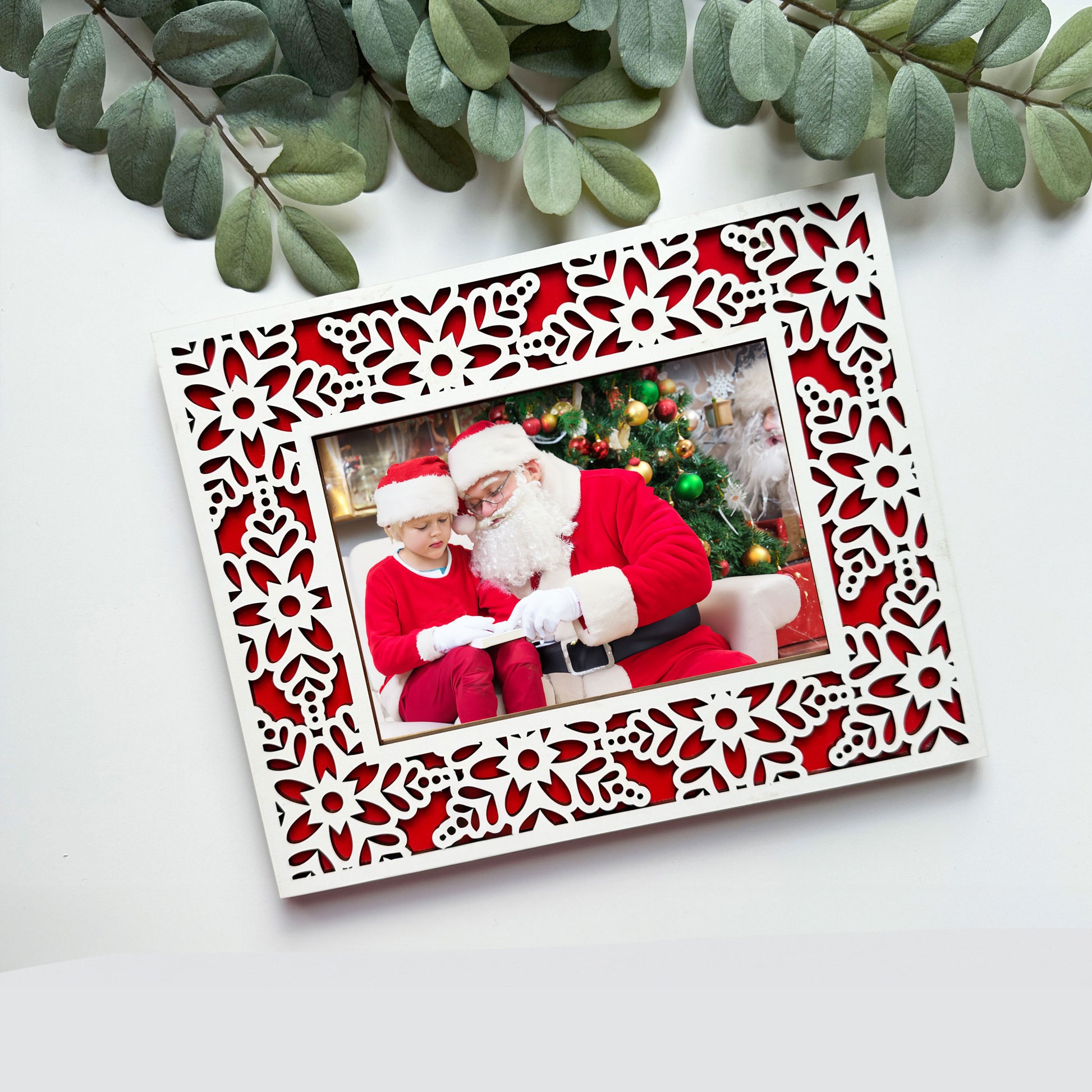 Decorative photo frame with a Christmas-themed picture of Santa Claus and a child, surrounded by green leaves.