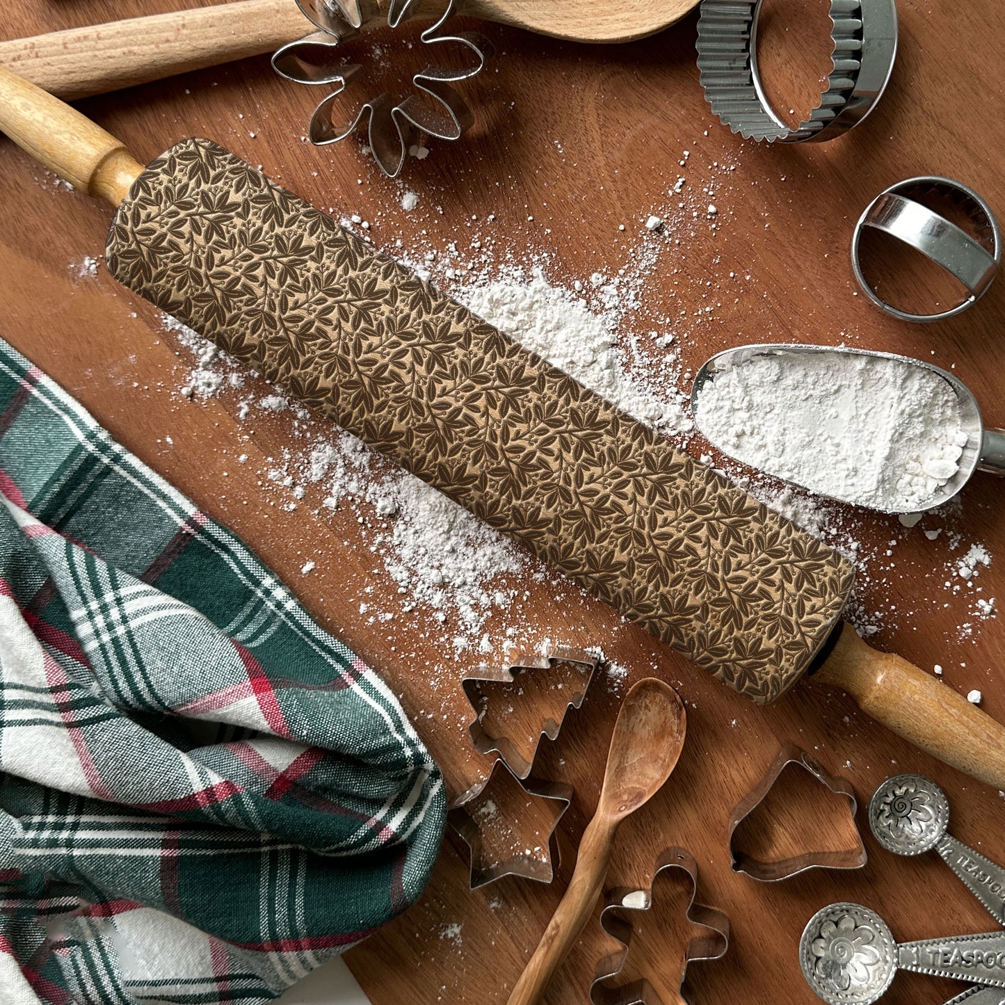 Baking tools including a textured rolling pin, cookie cutters, and flour on a wooden surface.