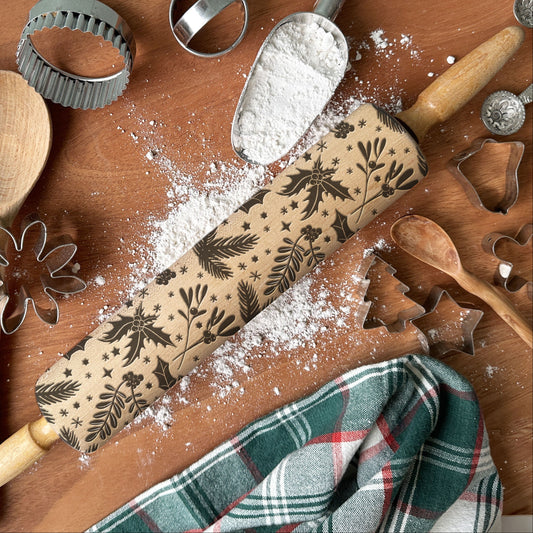 Decorative rolling pin with floral patterns on a wooden surface with baking tools and flour.