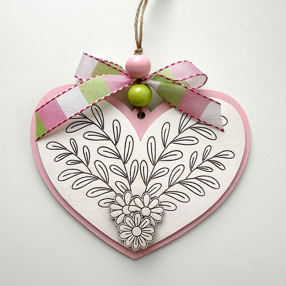 Heart-shaped decorative item with floral patterns, a bow, and a green bead on a white background