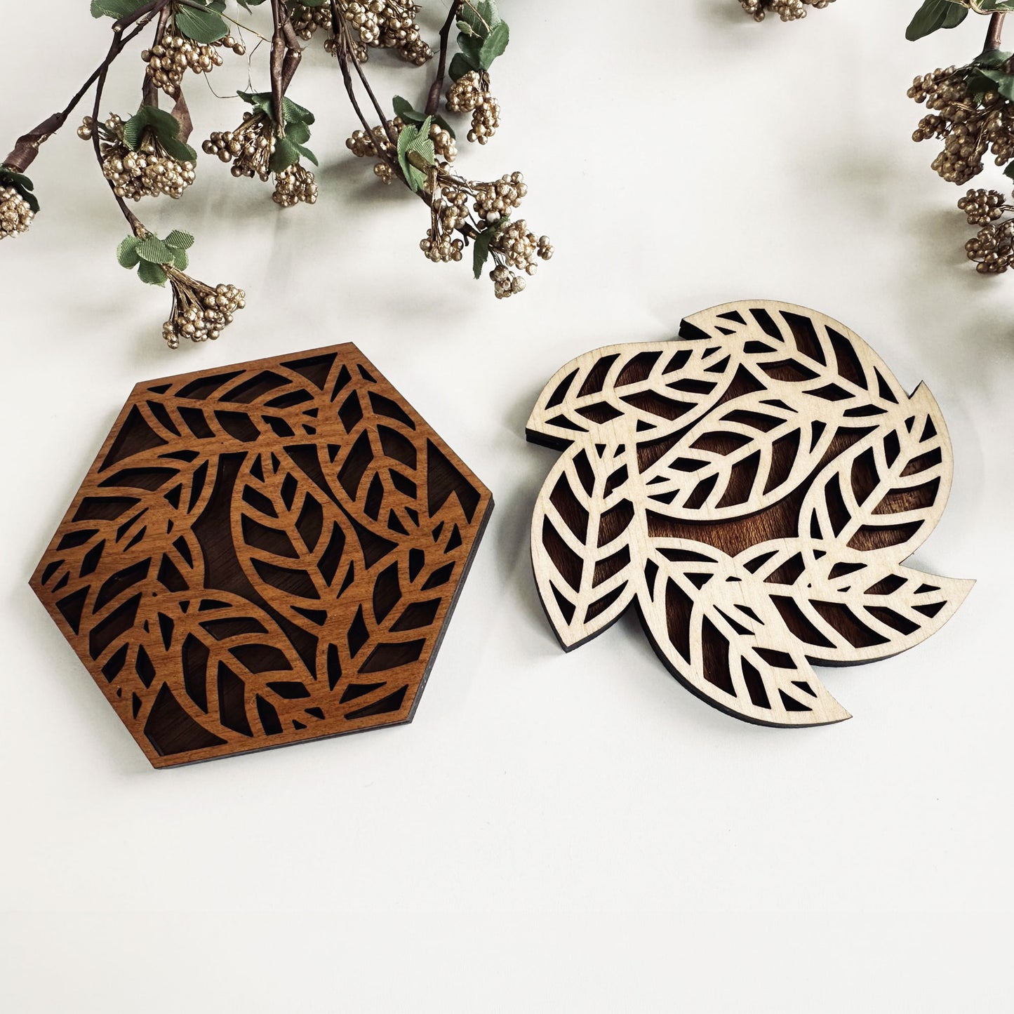 Two wooden coasters with leaf patterns on a white surface with decorative branches.