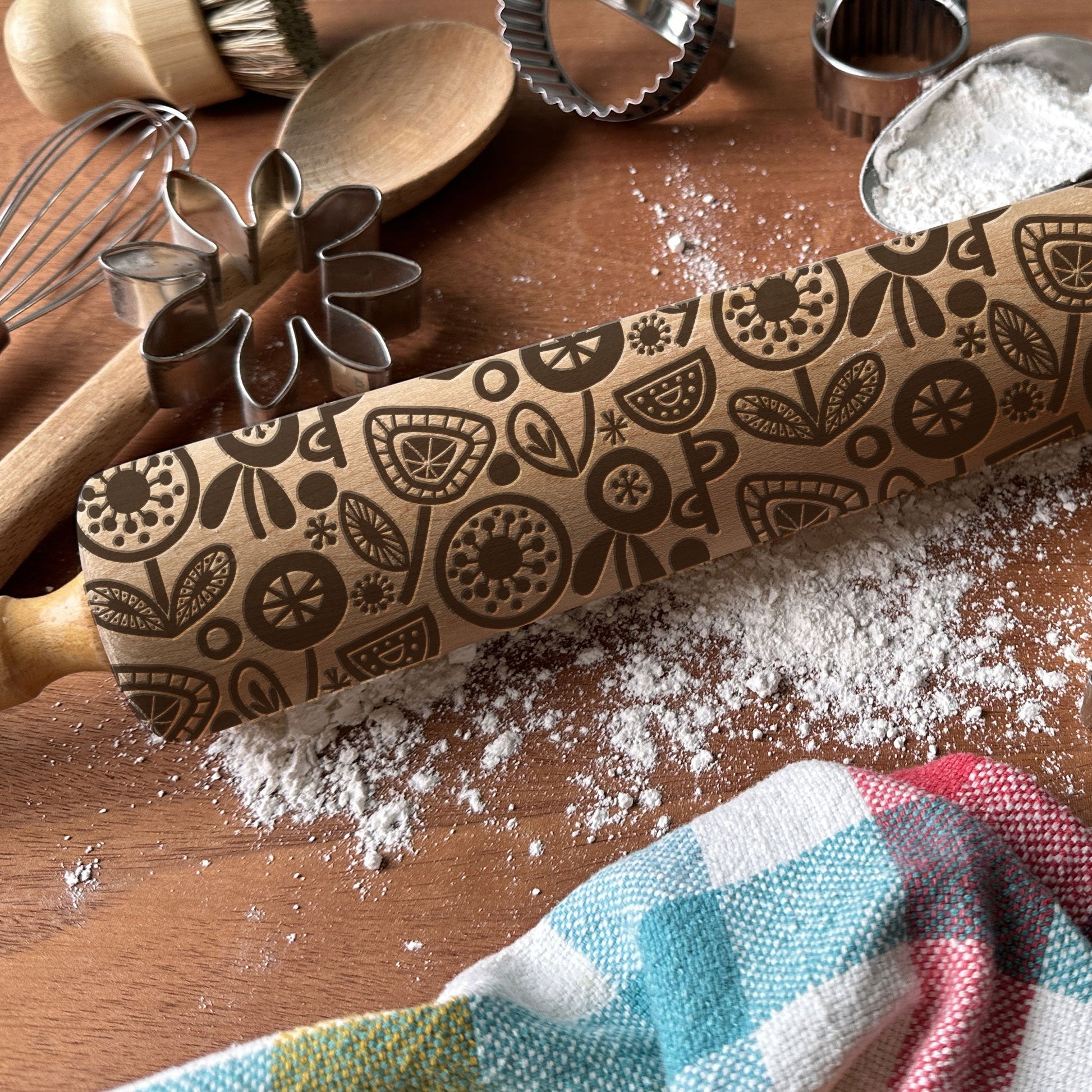 Decorative rolling pin with floral patterns on a wooden surface with flour and baking tools.