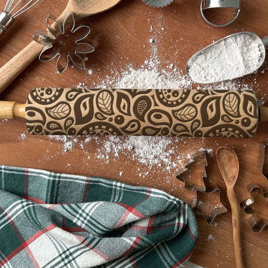 Decorative rolling pin with leaf pattern on a wooden surface with baking tools and flour.
