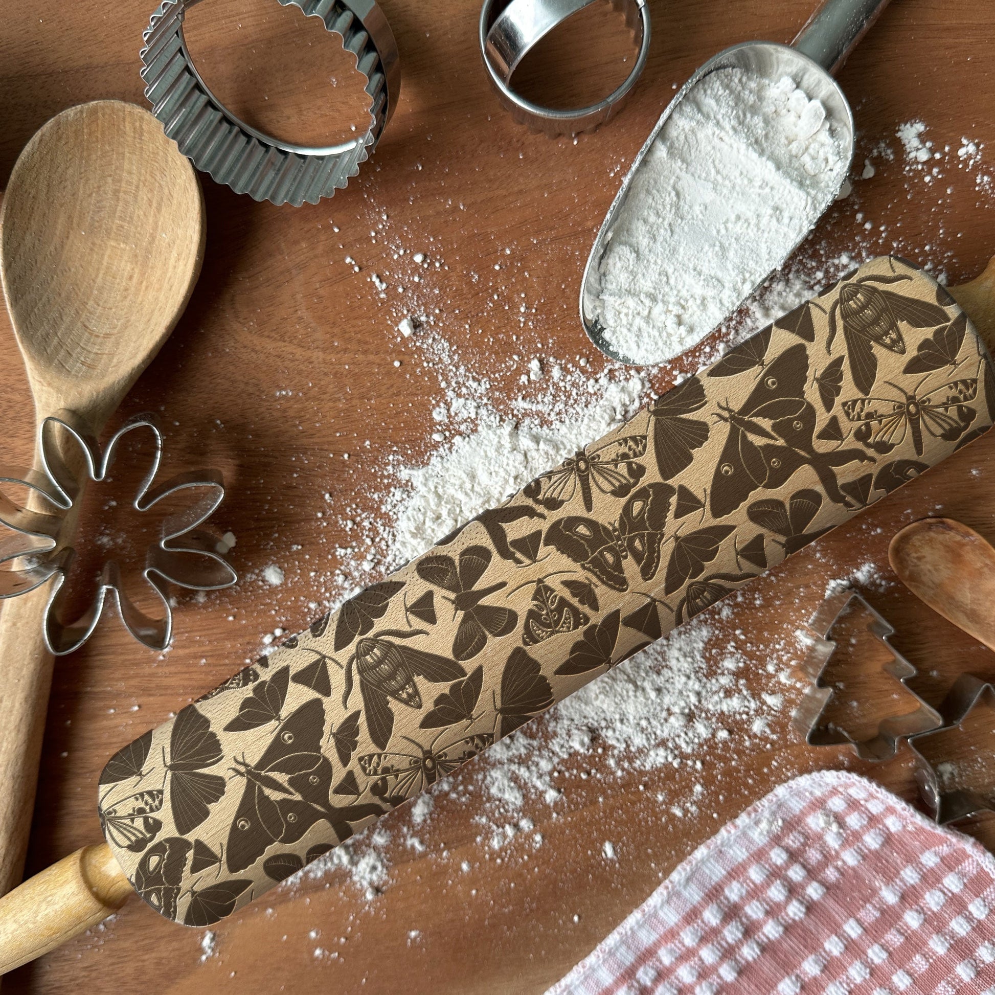 Decorative rolling pin with butterfly patterns on a wooden surface with flour and baking tools.