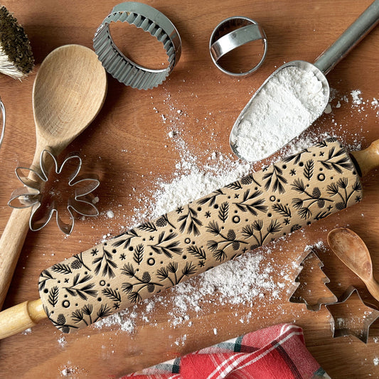 Decorative rolling pin with Christmas patterns on a wooden surface with baking tools.