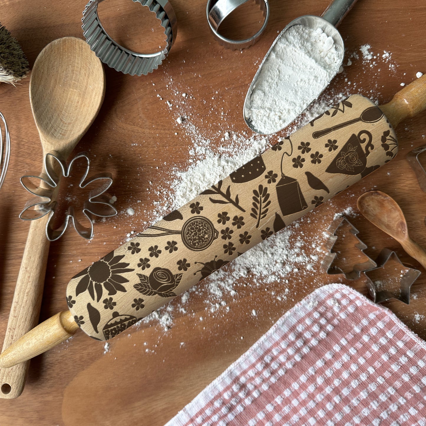 Decorative rolling pin with embossed patterns on a wooden surface with flour and baking tools.