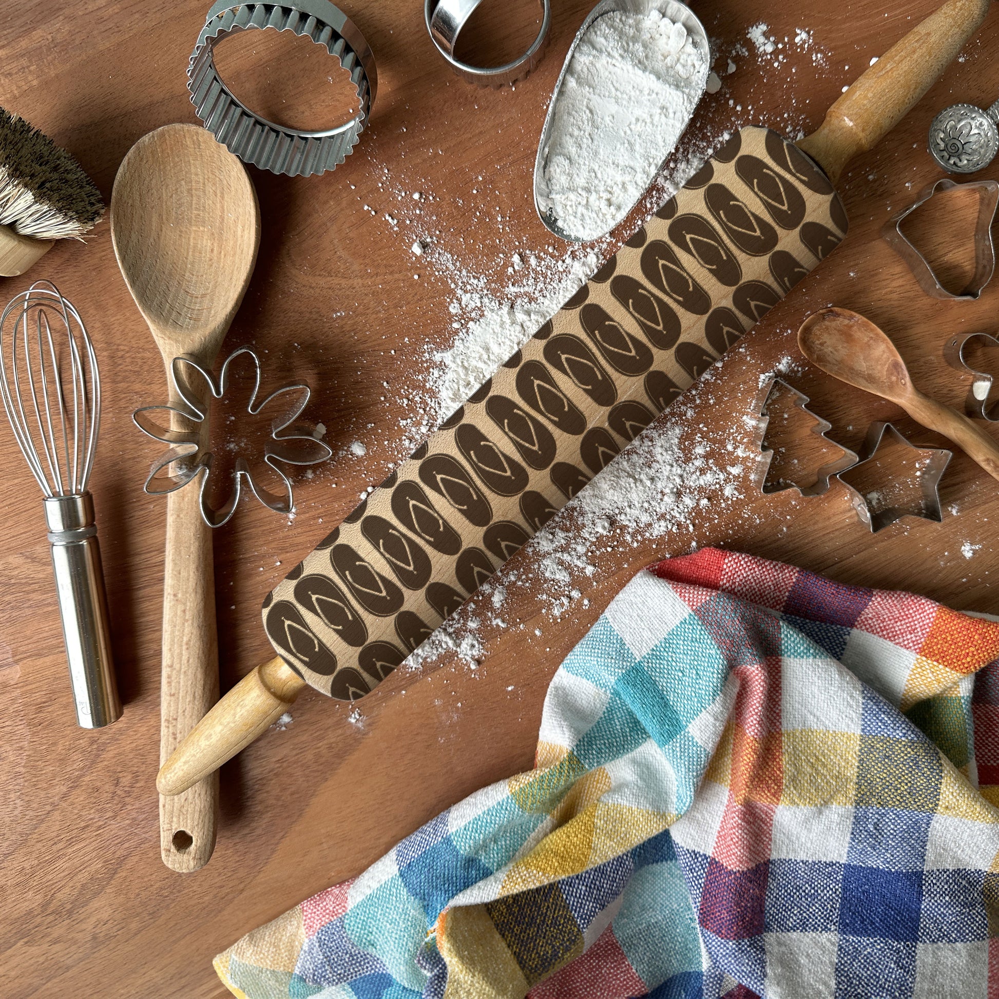 Wooden kitchen utensils including a rolling pin, spatula, and cookie cutters on a wooden surface with flour.