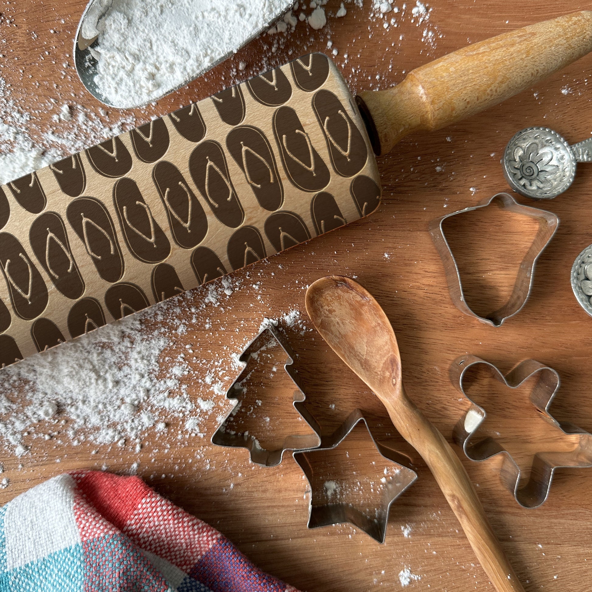 Baking tools including a rolling pin, cookie cutters, and a wooden spoon on a wooden surface with flour.