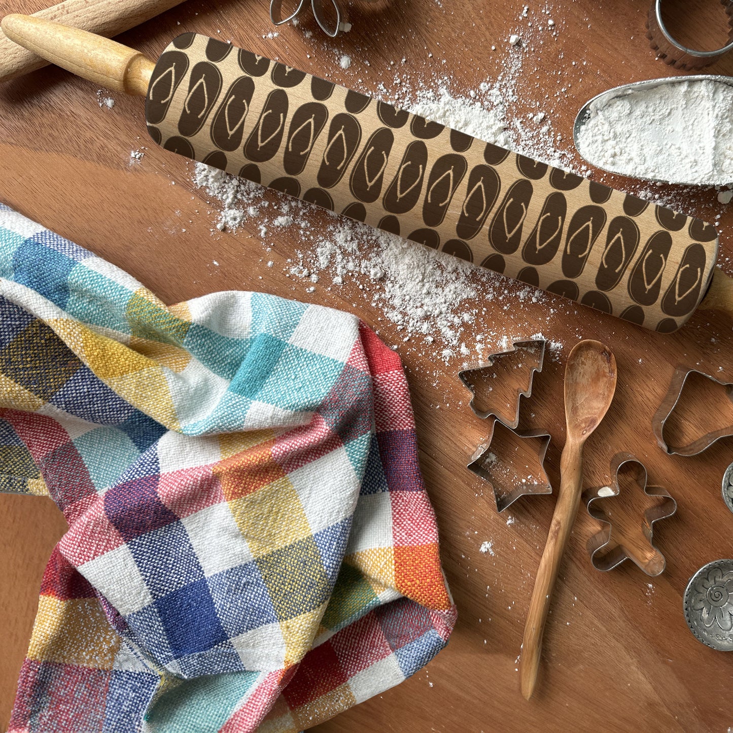 Wooden rolling pin with decorative pattern on a wooden surface with cookie cutters and a colorful towel.