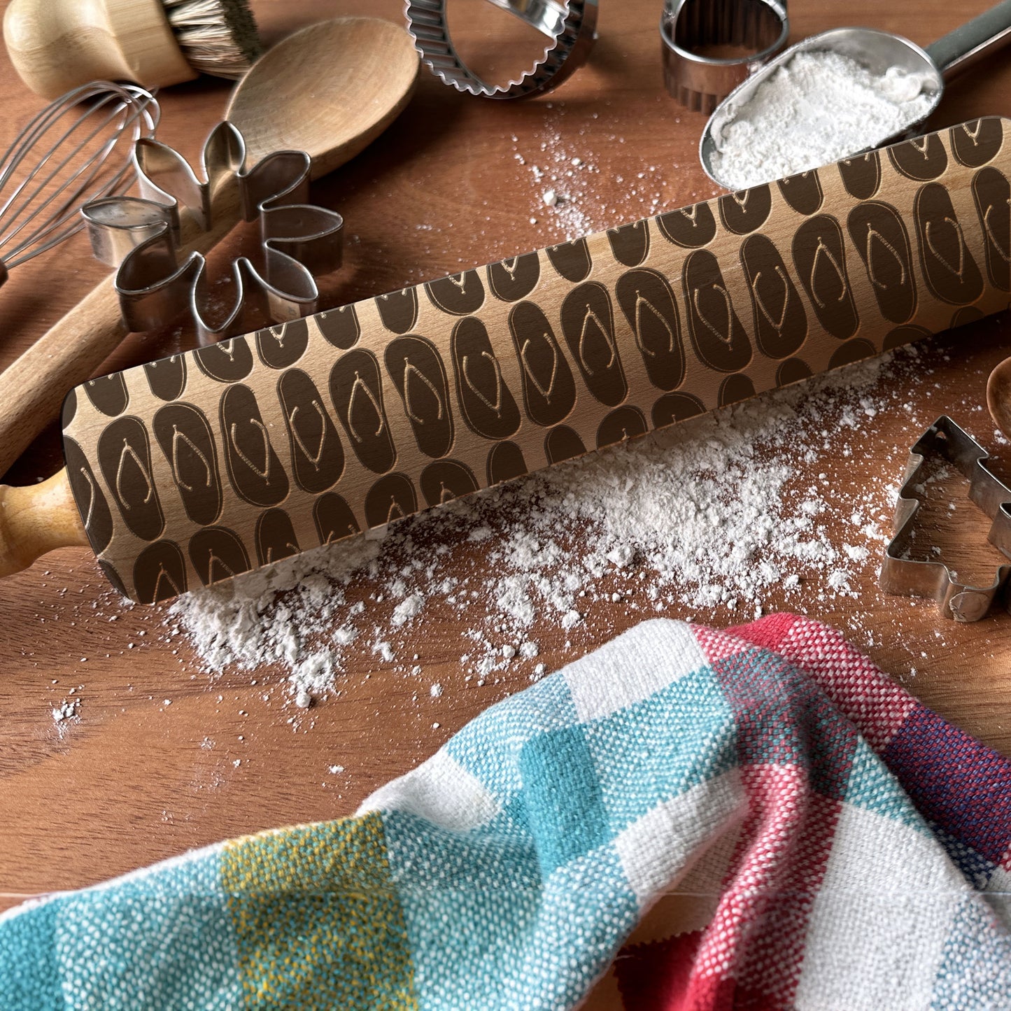 Patterned rolling pin on a wooden surface with flour and kitchen tools.