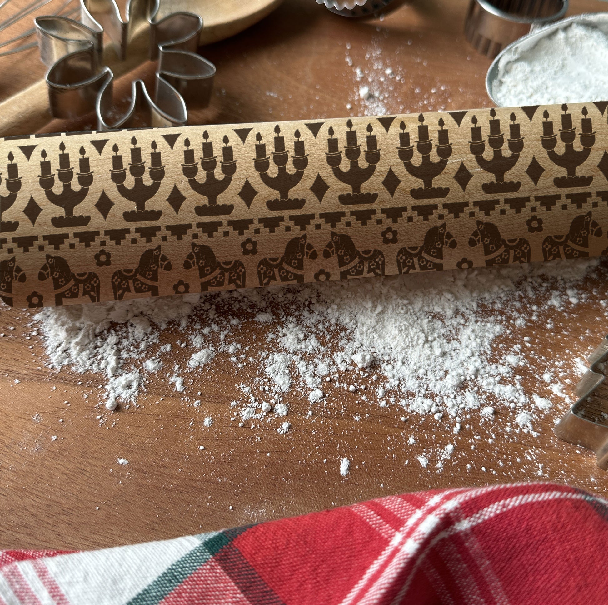Decorative wooden rolling pin on a wooden surface with flour and cookie cutters.