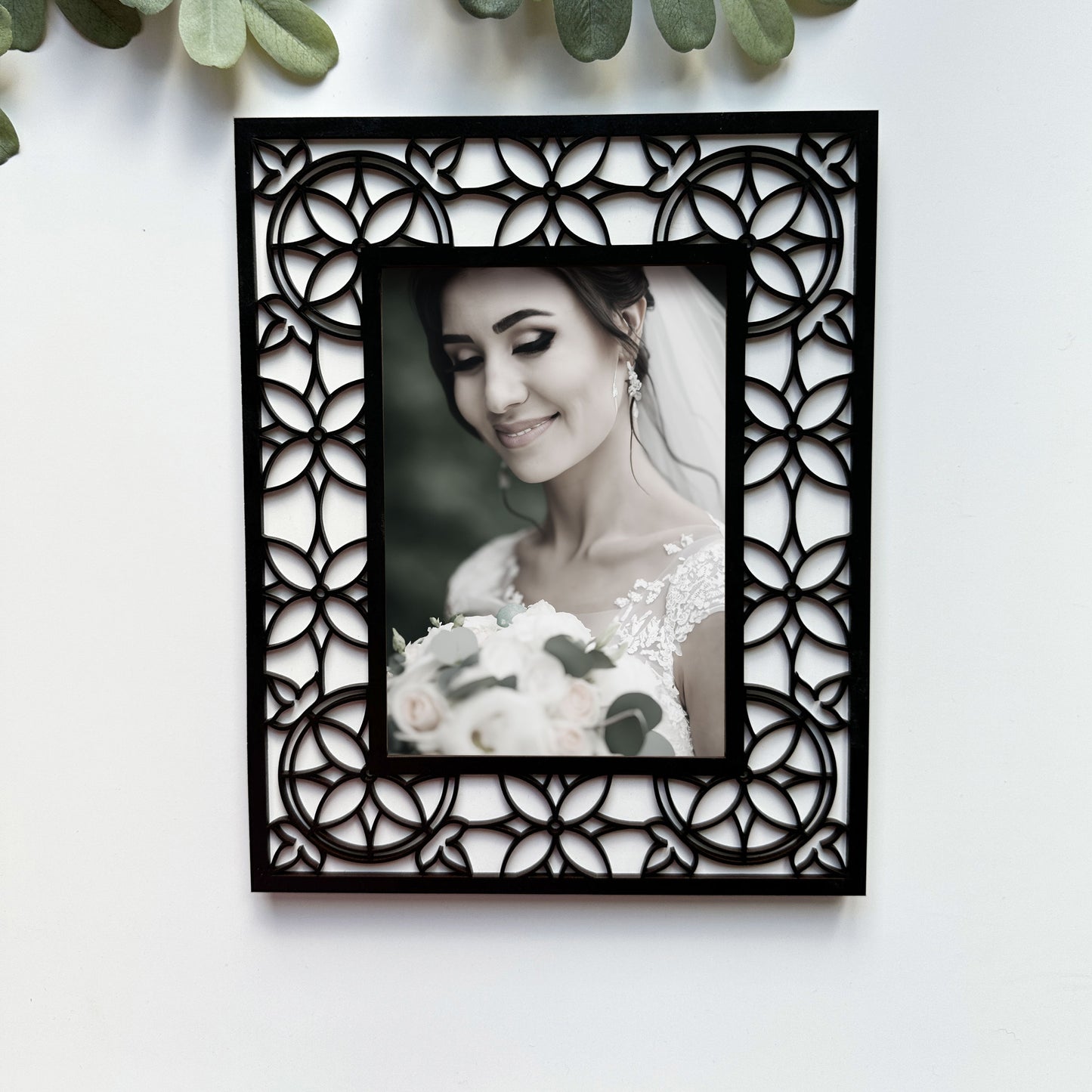 Decorative black frame with intricate patterns holding a photo of a bride on a white background.