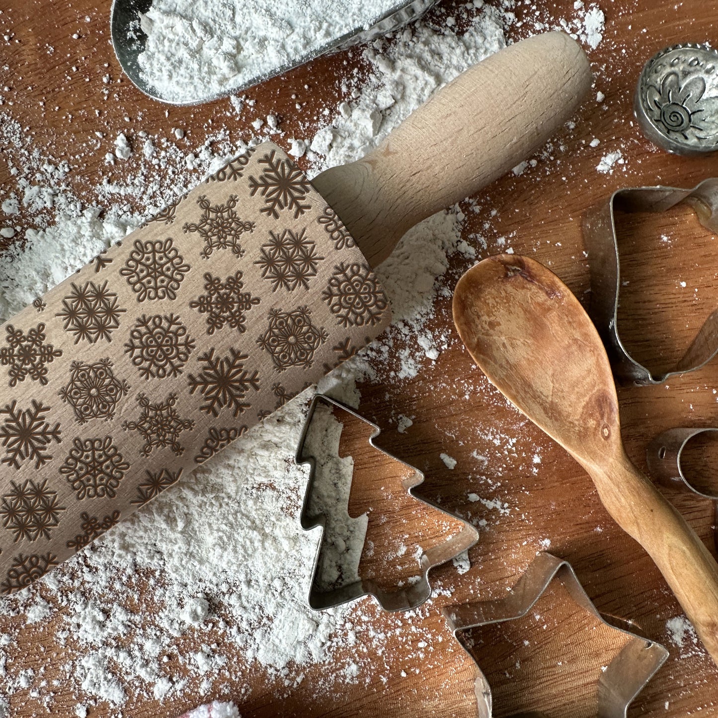 Wooden rolling pin with snowflake patterns on a flour-dusted surface with cookie cutters.