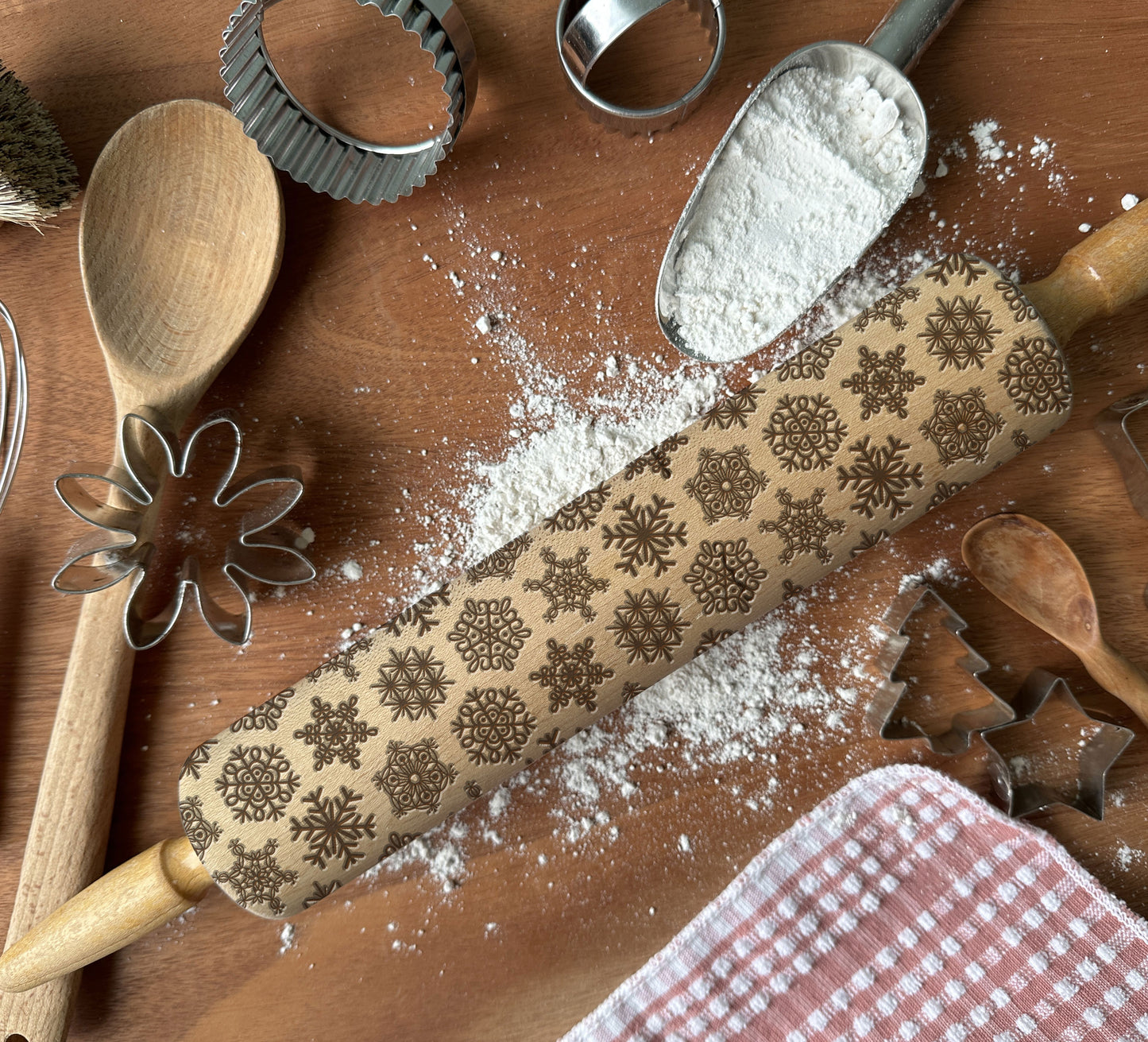 Decorative rolling pin with snowflake patterns on a wooden surface with flour and baking tools.