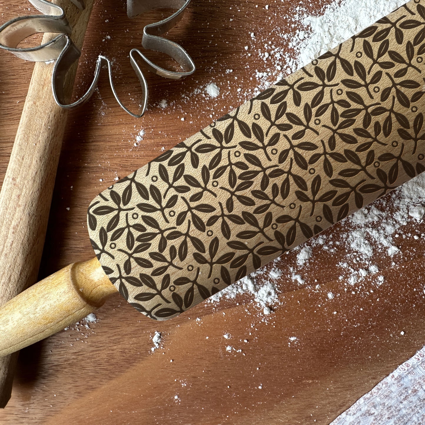 Wooden rolling pin with embossed leaf pattern on a wooden surface with flour.