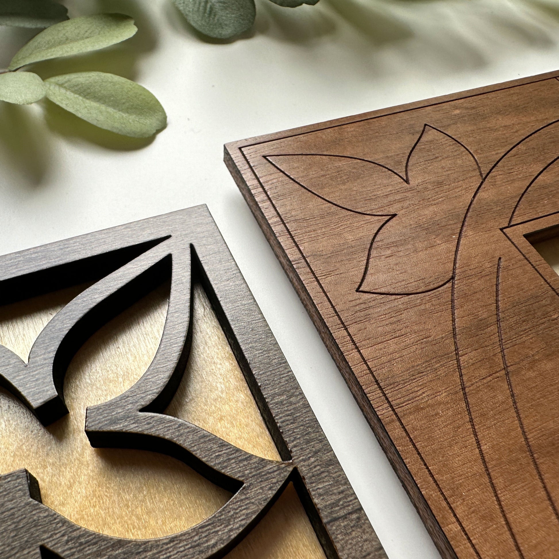 Close-up of two wooden decorative panels with intricate carvings on a light background.