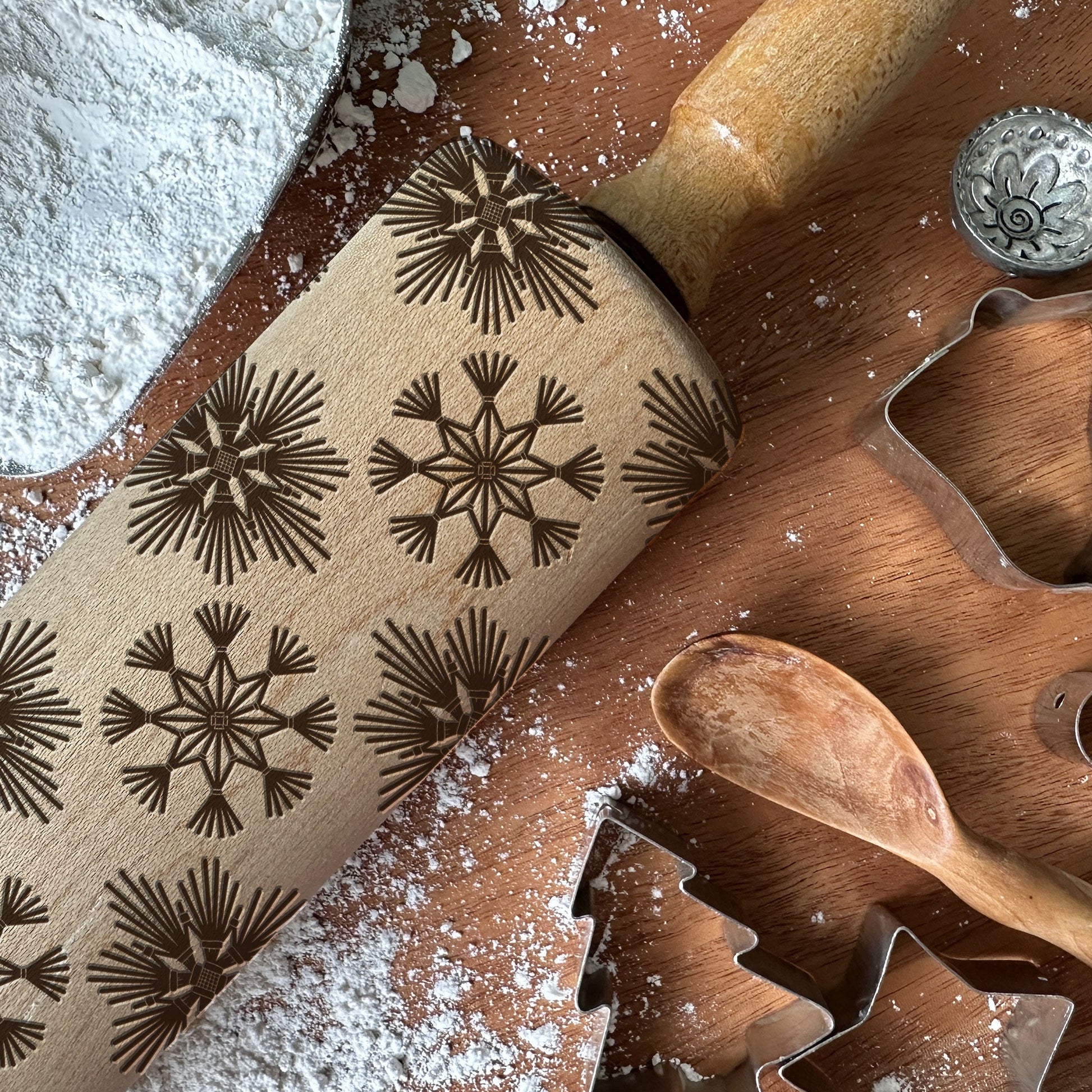 Rolling pin with snowflake patterns and cookie cutters on a wooden surface with flour.