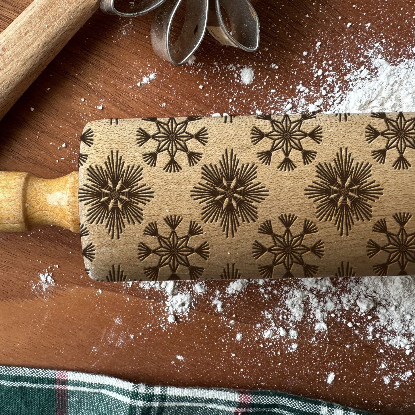 Rolling pin with snowflake pattern on a wooden surface with flour.