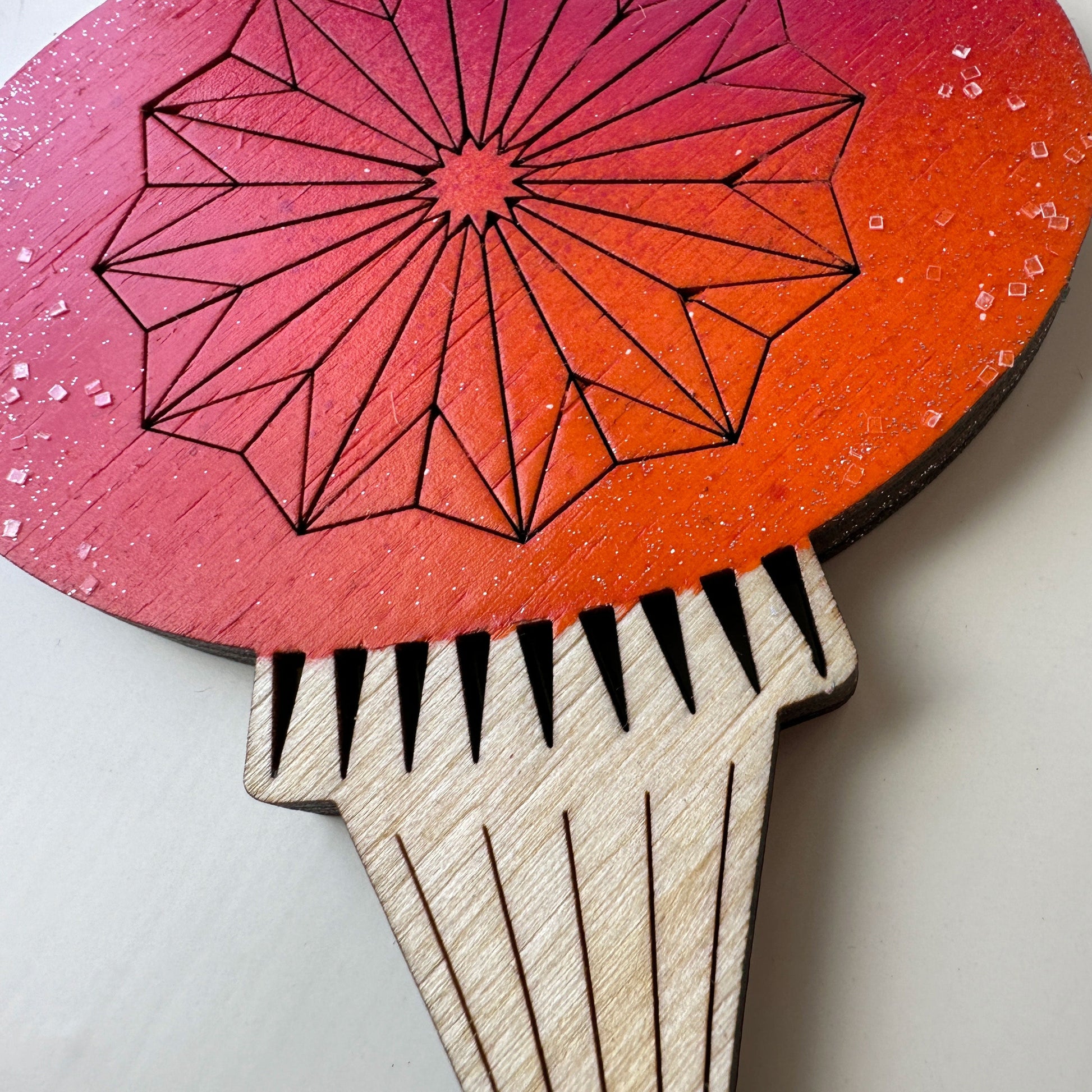 Wooden paddle with geometric design on a pink and red background
