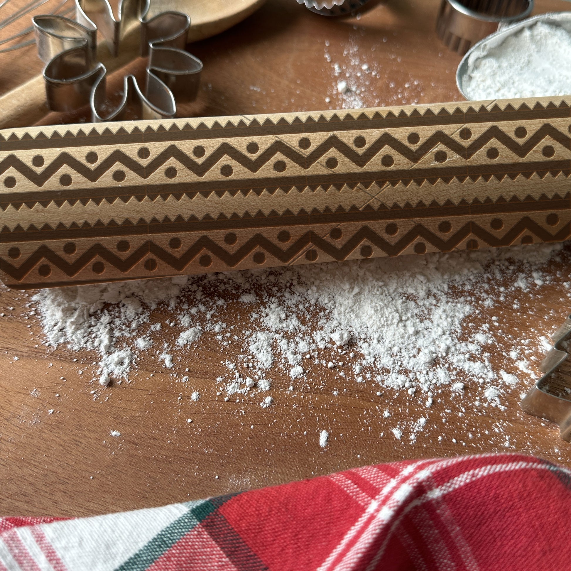 Decorative wooden rolling pin on a wooden surface with flour and cookie cutters.